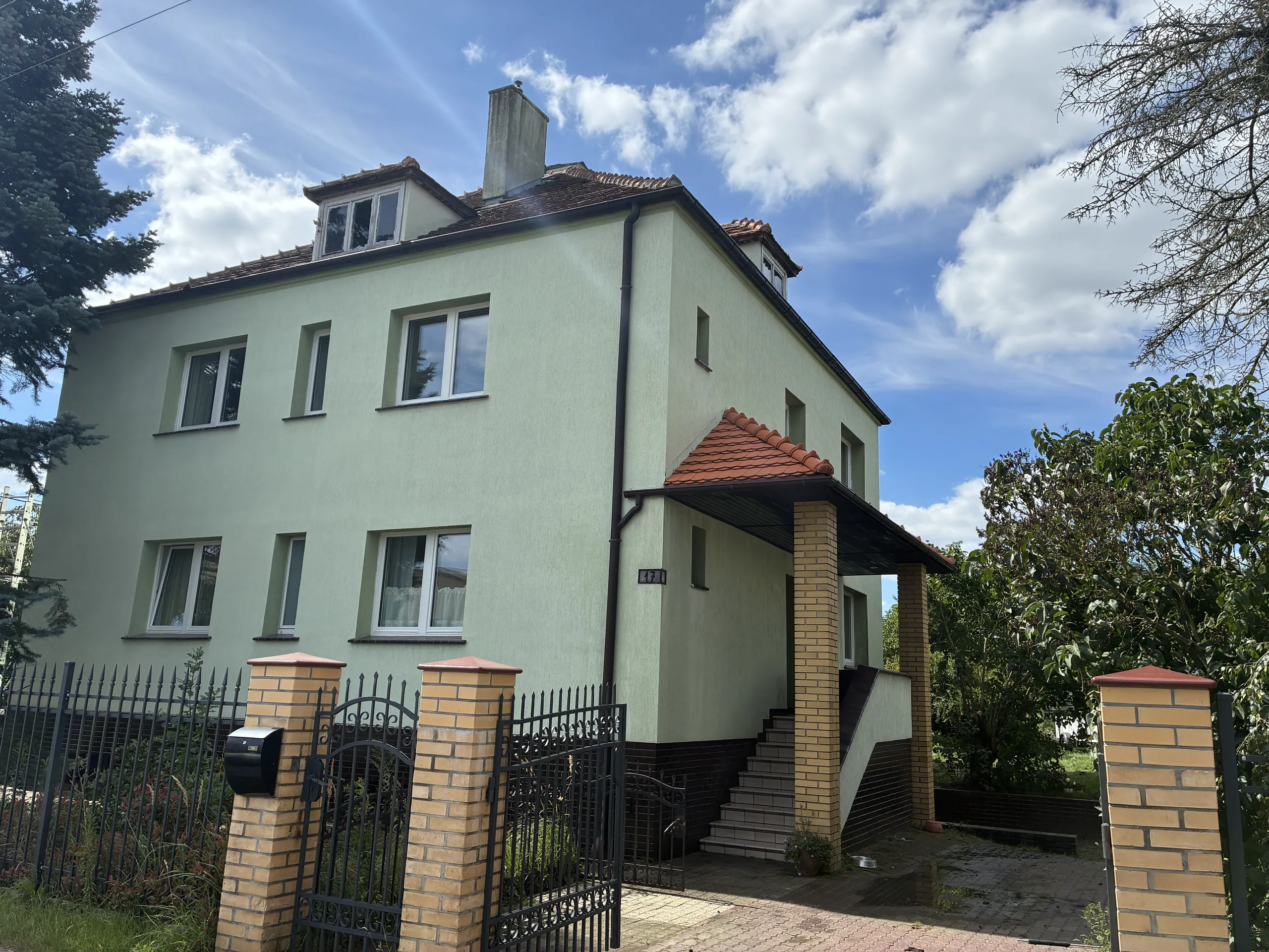 Elewacja domu z zielonym tynkiem, zewnętrzne schody i kostka brukowa przy wejściu