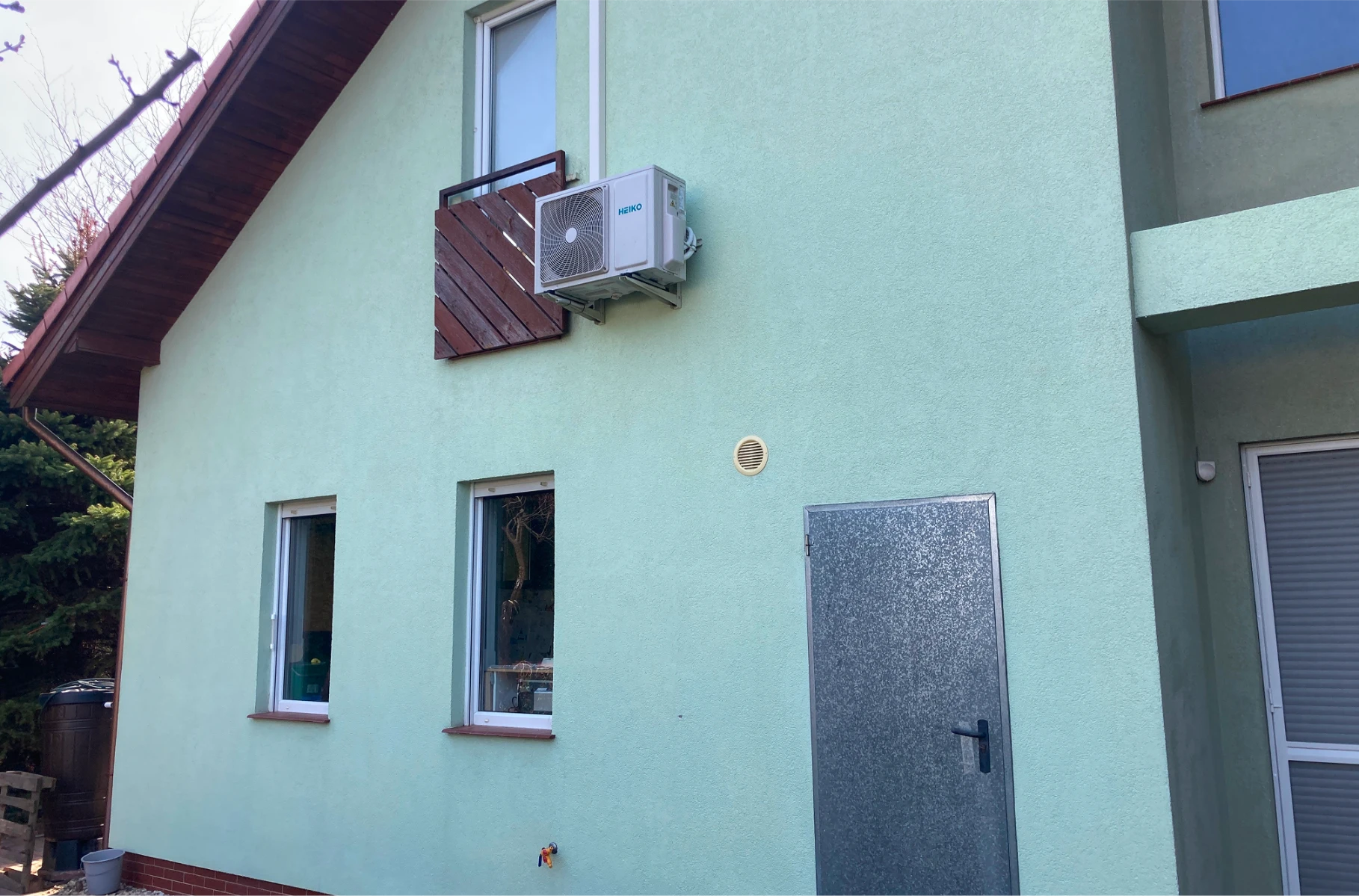 Elewacja domu w kolorze jasnej zieleni z dwoma oknami, metalowymi drzwiami i jednostką klimatyzacyjną